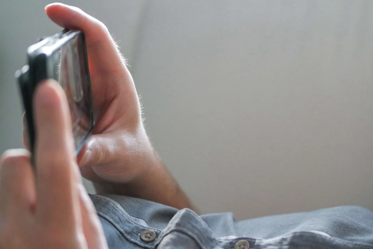 Primer plano de manos masculinas usando un teléfono móvil para ver contenido en plataformas digitales.