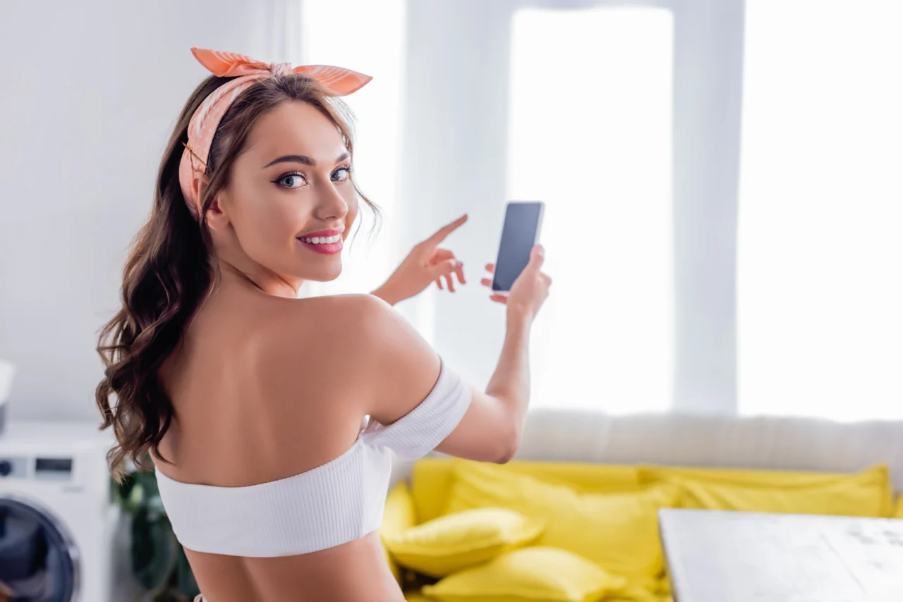 Modelo joven sonriente mostrando su teléfono, ilustrando cuánto cuesta OnlyFans para fans y creadores.