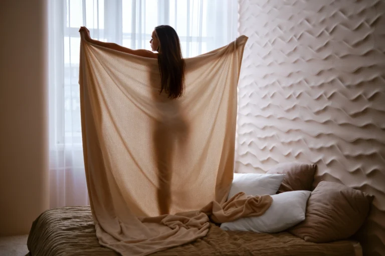 Chica posando tras una sábana en una habitación, contenido artístico que refleja cuánto cuesta OnlyFans y el tipo de publicaciones que se ofrecen.